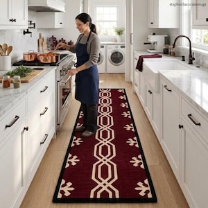 May include: A burgundy kitchen runner rug with a geometric and leaf pattern. The rug has a black border and is placed in a kitchen with white cabinets and a woman cooking. The rug measures approximately 2.5 feet wide.