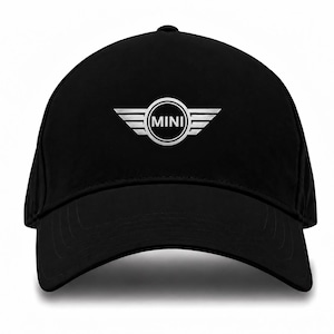 Könnte beinhalten: Eine schwarze Baseballkappe mit einem mittig platzierten, silberfarbenen MINI-Logo. Das Logo besteht aus einem kreisförmigen Emblem mit dem Wort MINI in der Mitte, flankiert von zwei stilisierten Flügeln auf beiden Seiten. Die Kappe hat einen Schirm.