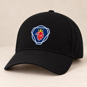 May include: A black baseball cap featuring a centered emblem of a red griffin with a yellow crown, enclosed within a blue shield shape outlined in white. The cap has a structured crown, a curved brim with stitching, and a button on the top.