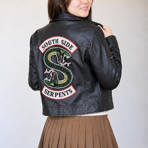 May include: A black leather jacket featuring a large embroidered patch on the back. The patch displays a green snake coiled into an S shape with red accents and the text SOUTH SIDE SERPENTS in white lettering on a red background.