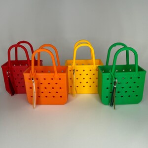 May include: Four colorful tote bags in red, orange, yellow, and green. Each bag has a square shape, a handle, and a tassel. The bags have a perforated design with small, evenly spaced holes.
