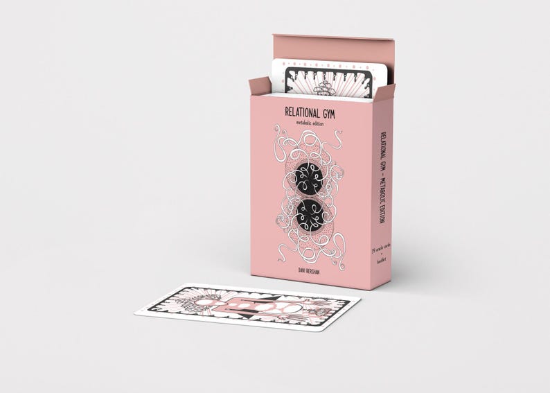 Pode incluir: Uma caixa de cartas rosa com a inscri&ccedil;&atilde;o "RELATIONAL GYM" e um baralho de cartas dentro. Uma carta est&aacute; colocada na frente. A caixa apresenta um design &uacute;nico com dois c&iacute;rculos pretos e um desenho linear branco. As cartas t&ecirc;m um design a preto e branco.