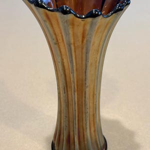 May include: A decorative iridescent glass vase with a ruffled rim. The vase has vertical ridges and a flared shape. The colors include gold, orange, and hints of blue and purple. The base and rim are dark.