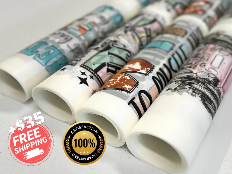 May include: Rolled decorative paper with various designs, including text and graphics. The designs feature a mix of colors, including teal, brown, and black. The paper rolls are white with the designs printed on them. The image shows several rolls.
