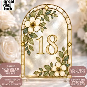 Op de afbeelding: Een boogvormig tafelnummerbord met het getal 18 in een goudomlijnd lettertype. Het ontwerp bevat witte bloemen en groene bladeren op een textuurrijke achtergrond met een gouden frame. Tekst: TABLE NUMBERS 1-35 INCLUDED SIZE 5x7, SVG+ PRINT READY PDF, PRINT READY PDF BLACK & WHITE, BEGINNERS PAINTING GUIDE PDF.