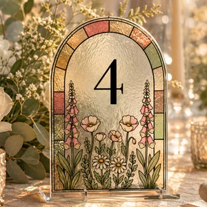 May include: An arched table number sign featuring the number 4 in black. The sign has a textured glass surface with a stained glass border in pastel tones and a printed illustration of pink foxgloves, white daisies, and light pink poppies.
