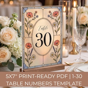 May include: A rectangular table number sign featuring a stained glass style design with floral illustrations of pink poppies, white daisies, and purple lavender. The center oval contains the text Table 30 in black font, set on a wooden base.