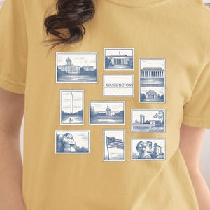 Könnte beinhalten: Senfgelbes T-Shirt mit einer blau-weißen Grafik von Wahrzeichen von Washington D.C. Das Design umfasst Illustrationen von Gebäuden, Denkmälern und den Text "WASHINGTONS" in einem rechteckigen Feld. Das Shirt besteht aus einem weichen, bequemen Material.