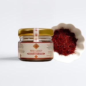 May include: A jar of Red Gold Reserve premium quality saffron with a gold lid and label. A small white bowl filled with red saffron threads is next to the jar. The jar is on a white surface.