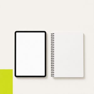 May include: A digital tablet with a black frame and a blank white screen positioned next to a white spiral-bound notebook with a black wire coil. The tablet and notebook are displayed against a plain, light-colored background.