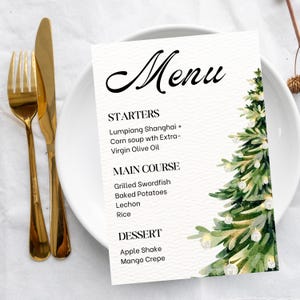May include: A white menu card with a watercolor Christmas tree design. The menu includes starters, main courses, and desserts. Gold-colored fork and knife are on the left side of the plate. The menu items are listed in black text.