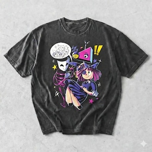 May include: Dark gray t-shirt featuring a colorful cartoon graphic. The graphic includes a girl in a blue dress, a masked figure, and a speech bubble with masks. The design also incorporates stars and geometric shapes.