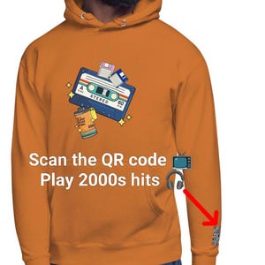 Puede incluir: Sudadera con capucha naranja con un gráfico de cinta de cassette retro, rollo de película y disquetes. El texto "Scan the QR code Play 2000s hits" está impreso en la parte delantera. Un código QR está en la manga.