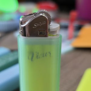 Może przedstawiać: Zbliżenie zielono-srebrnej zapalniczki. Na boku zapalniczki widnieje napis "Views" w kursywie. Górna część zapalniczki jest srebrna i ma nadruk marki "Scripto".