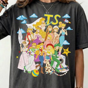 Puede incluir: Una camiseta gris carb&oacute;n con un estampado gr&aacute;fico colorido de varios personajes animados con diversos atuendos, incluyendo un traje espacial, ropa de vaquera y vestidos formales. El texto TS est&aacute; impreso en amarillo sobre los personajes.