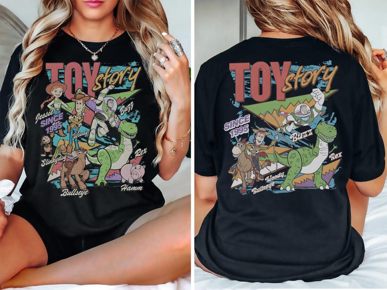 May include: A black t-shirt featuring a colorful graphic print of Toy Story characters including Woody, Buzz Lightyear, Jessie, Rex, Bullseye, Slinky Dog, and Hamm. The design includes the text Toy Story and Since 1995 with geometric shapes.