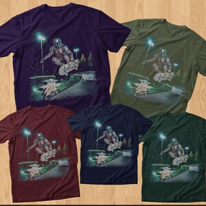 Op de afbeelding: Vijf T-shirts met korte mouwen in verschillende kleuren: paars, olijfgroen, bordeauxrood, marineblauw en donkergroen. Elk shirt heeft een afbeelding van een personage dat skateboardt met een klein groen wezen. Het ontwerp omvat een helling, bomen en straatverlichting.