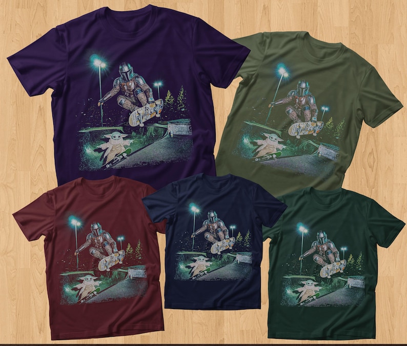 Op de afbeelding: Vijf T-shirts met korte mouwen in verschillende kleuren: paars, olijfgroen, bordeauxrood, marineblauw en donkergroen. Elk shirt heeft een afbeelding van een personage dat skateboardt met een klein groen wezen. Het ontwerp omvat een helling, bomen en straatverlichting.