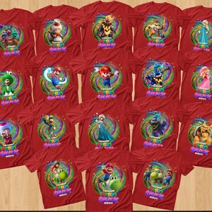 May include: A collection of red t-shirts featuring various characters from The Super Mario Bros. Movie. Each shirt displays a circular, swirling, colorful background graphic behind a specific character and the movie title text in a stylized font.