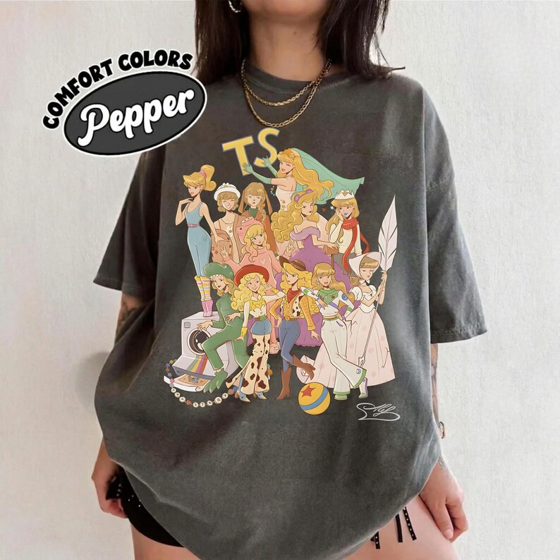 Puede incluir: Una camiseta gris carb&oacute;n con un estampado gr&aacute;fico de varios personajes animados con diversos atuendos. El texto "COMFORT COLORS" y "Pepper" aparece en la esquina superior izquierda, mientras que las letras "TS" est&aacute;n impresas sobre los personajes.