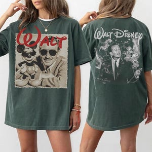 May include: A dark green oversized t-shirt featuring a graphic on the front and back. The front displays a sepia-toned image of Walt Disney and Mickey Mouse wearing sunglasses with the red text Walt. The back shows Walt Disney with Mickey Mouse.