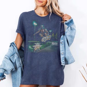 Op de afbeelding: Marineblauw T-shirt met een afbeelding van The Mandalorian en Grogu die skaten in een skatepark. Het ontwerp heeft een groen-wit kleurenschema met een nachtsc&egrave;ne. Het shirt is een comfortabele, casual stijl.