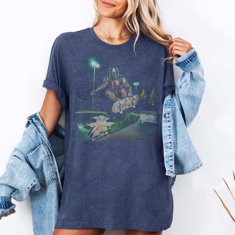 Op de afbeelding: Marineblauw T-shirt met een afbeelding van The Mandalorian en Grogu die skaten in een skatepark. Het ontwerp heeft een groen-wit kleurenschema met een nachtsc&egrave;ne. Het shirt is een comfortabele, casual stijl.