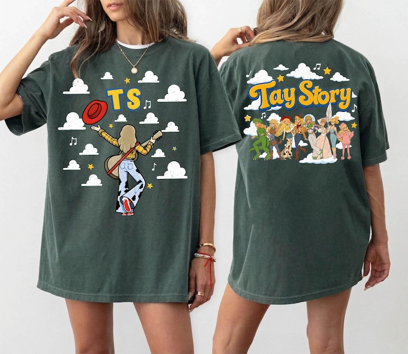 May include: A dark green short-sleeve t-shirt featuring a graphic print. The front displays the text TS with a figure holding a guitar and hat amidst clouds. The back shows the text Tay Story with a group of illustrated figures and clouds.