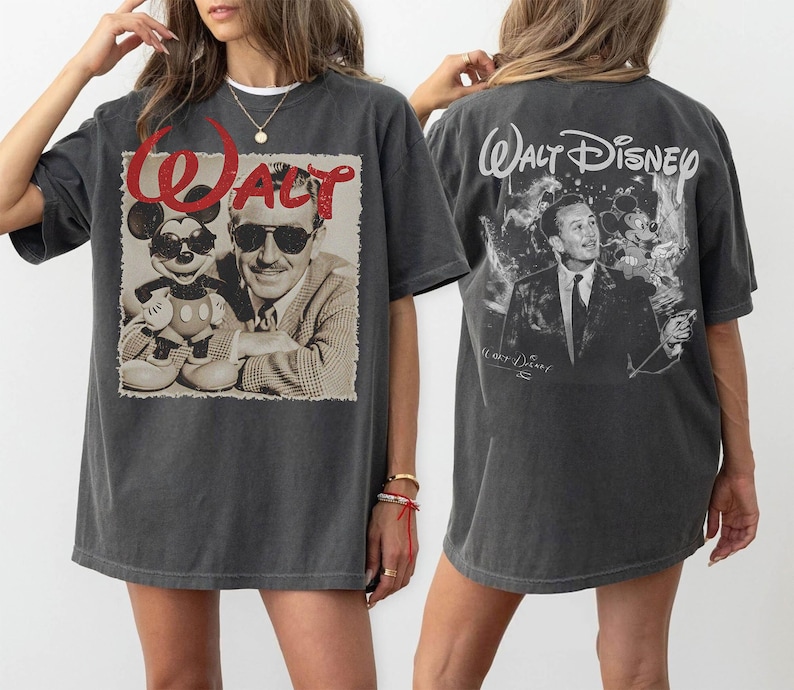 May include: A charcoal gray short-sleeve t-shirt featuring a front graphic of Walt Disney and Mickey Mouse wearing sunglasses with the red text Walt. The back displays a black and white graphic of Walt Disney and Mickey Mouse with the text Walt Disney.