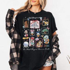 Może przedstawiać: Czarny t-shirt z długim rękawem z kolorowym kolażem postaci i zabytk&oacute;w Disneya. Projekt zawiera Myszkę Miki, Minnie, Kaczora Donalda i Goofy'ego, z tekstem "Walt Disney World" i "2026". Fraza "The Most Magical Place on Earth" jest r&oacute;wnież obecna.