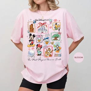 Może przedstawiać: Jasnor&oacute;żowa koszulka z kolorową grafiką przedstawiającą r&oacute;żne postacie i zabytki Disneya. Widoczny jest napis "Walt Disney World" i "The Most Magical Place on Earth". Widoczny jest r&oacute;wnież rok "2026".