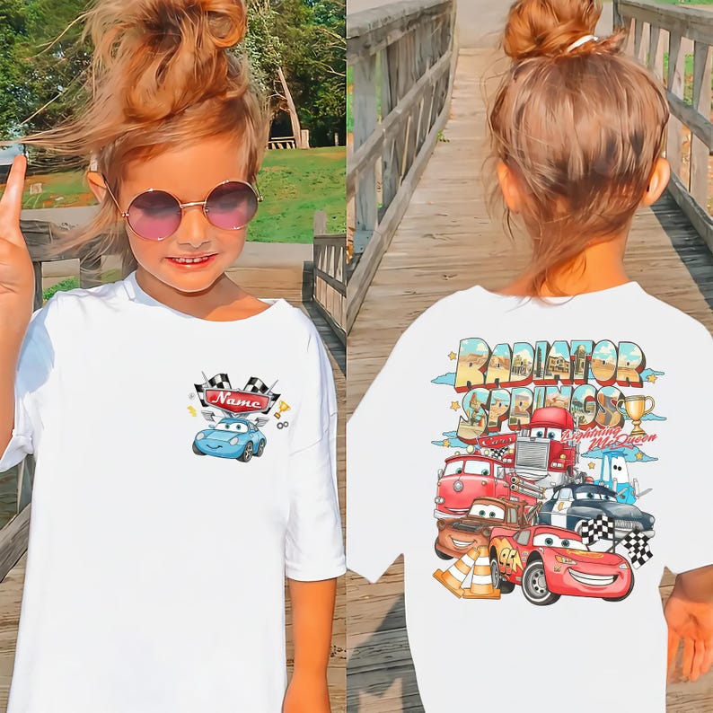 Puede incluir: Una camiseta blanca con un peque&ntilde;o gr&aacute;fico en el pecho de un coche azul con una bandera a cuadros y el texto Name. La parte posterior de la camiseta muestra un gr&aacute;fico grande y colorido de Radiator Springs con Lightning McQueen y amigos.