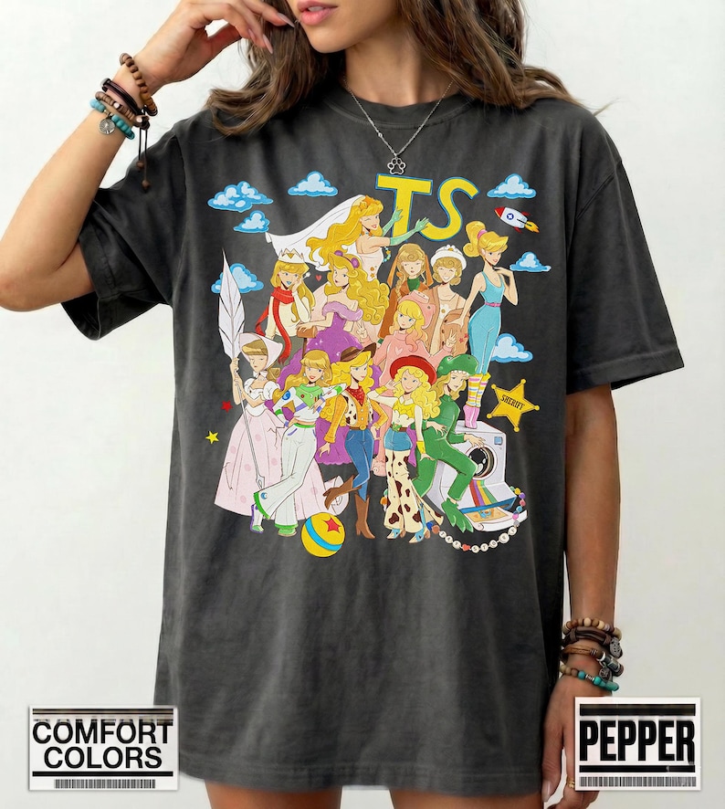 Puede incluir: Una camiseta gris carb&oacute;n con un estampado gr&aacute;fico colorido de varios personajes animados con diversos atuendos, incluyendo un traje espacial, ropa de vaquera y vestidos formales. El texto TS est&aacute; impreso en amarillo sobre los personajes.
