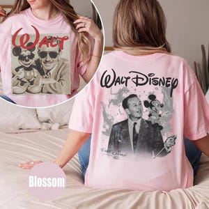 May include: A light pink t-shirt featuring a black and white graphic of Walt Disney and Mickey Mouse. The back displays the text Walt Disney above the graphic, while the front circular inset shows the same characters with the red text Walt.