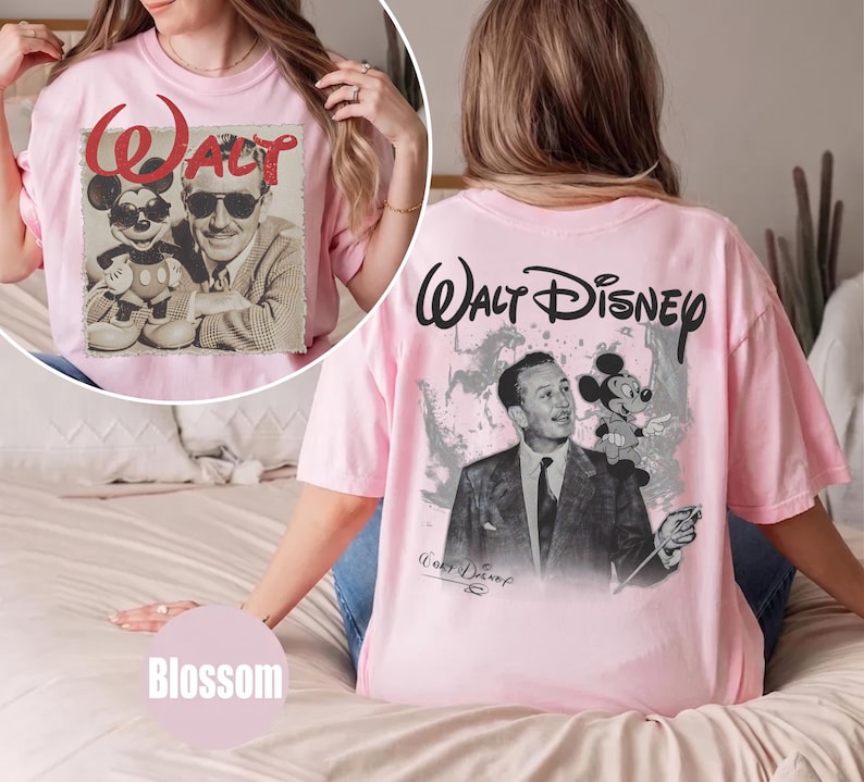 May include: A light pink t-shirt featuring a black and white graphic of Walt Disney and Mickey Mouse. The back displays the text Walt Disney above the graphic, while the front circular inset shows the same characters with the red text Walt.