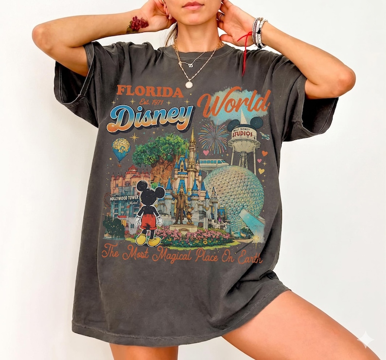 May include: A charcoal gray short-sleeve t-shirt featuring a colorful graphic print of Florida Disney World. The design includes Mickey Mouse, the castle, the Epcot sphere, and the text Florida Est. 1971 Disney World The Most Magical Place On Earth.