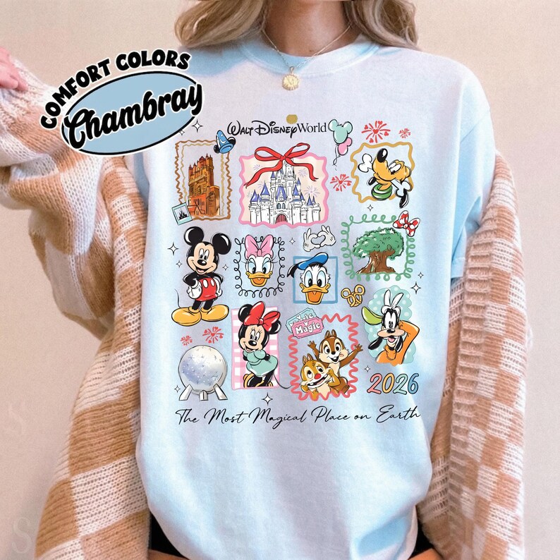 Może przedstawiać: Jasnoniebieska koszulka z kolorową grafiką Disney World. Projekt zawiera r&oacute;żne postacie i zabytki Disneya, z tekstem "Walt Disney World" i "2026". Koszulka zawiera r&oacute;wnież napis "The Most Magical Place on Earth".