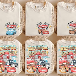 Puede incluir: Una colecci&oacute;n de camisetas color crema con estampados gr&aacute;ficos. La fila superior muestra personajes de coches individuales con banderas a cuadros y el texto Name. La fila inferior muestra un gran gr&aacute;fico de Radiator Springs con varios coches.
