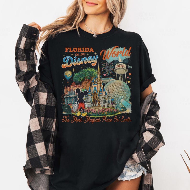 May include: A black t-shirt featuring a colorful graphic of Florida Disney World with the text Florida Est. 1971 Disney World and The Most Magical Place On Earth. The design includes a castle, Mickey Mouse, a water tower, and fireworks.