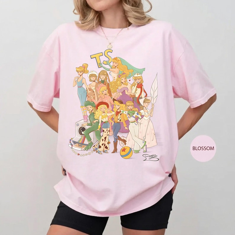 Puede incluir: Una camiseta de color rosa claro con un estampado gr&aacute;fico de varios personajes femeninos animados con diversos atuendos, incluyendo un sombrero de vaquero y un traje espacial, con las letras TS en la parte superior y una pelota colorida abajo.