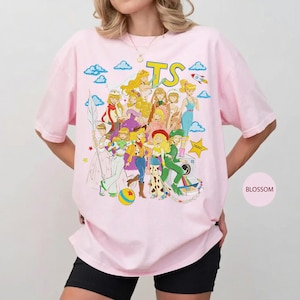 Puede incluir: Una camiseta de manga corta de color rosa claro con un gran estampado gr&aacute;fico de varios personajes animados con diversos atuendos. El texto TS est&aacute; impreso en amarillo en la parte superior. El dise&ntilde;o incluye nubes, un cohete y una estrella.