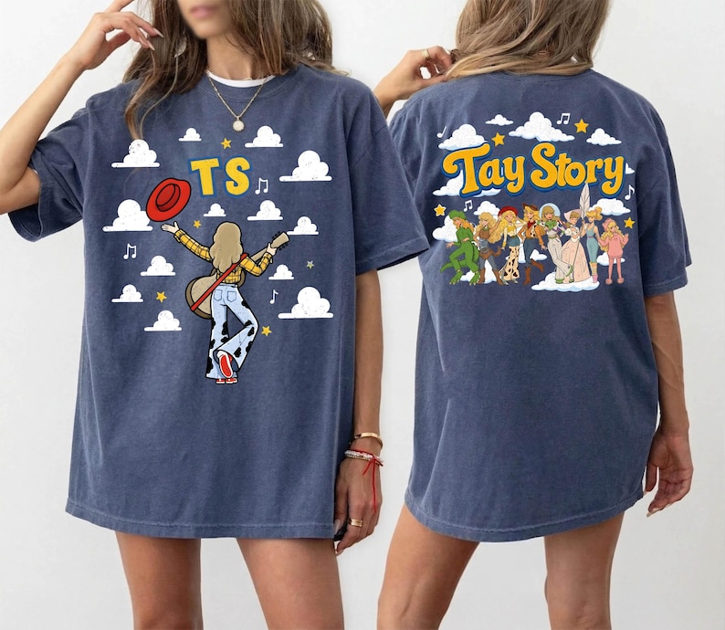 May include: A navy blue t-shirt featuring a graphic print. The front shows a person with a guitar, a red hat, and the text TS against a cloud background. The back displays a group of figures and the text Tay Story with clouds and stars.