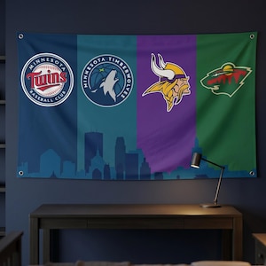 Puede incluir: Una gran bandera de pared con cuatro paneles verticales que muestran los logotipos de los equipos deportivos de Minnesota: béisbol de los Twins, baloncesto de los Timberwolves, fútbol americano de los Vikings y hockey de los Wild. La bandera tiene una silueta de paisaje urbano en la parte inferior.