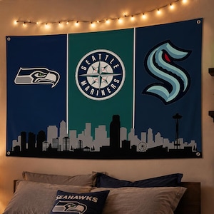 Puede incluir: Un tapiz de pared rectangular con tem&aacute;tica deportiva de Seattle, con un dise&ntilde;o de paneles verticales en azul oscuro, verde azulado y azul oscuro. Muestra el logotipo de los Seattle Seahawks, el logotipo de la br&uacute;jula de los Seattle Mariners y el logotipo del Seattle Kraken sobre un horizonte urbano negro.