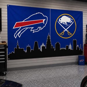 Peut inclure: Une grande bannière murale rectangulaire bleue présentant le logo blanc des Buffalo Bills à gauche et le logo jaune et blanc des Buffalo Sabres à droite, avec une silhouette noire de ligne d'horizon urbaine imprimée en bas.