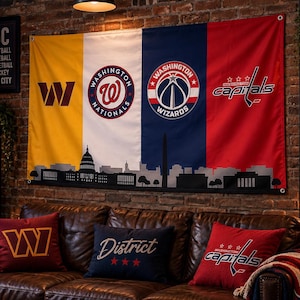 May include: A large horizontal wall banner featuring the logos of the Washington Commanders, Nationals, Wizards, and Capitals over a black silhouette of the Washington D.C. skyline. The banner is divided into yellow, white, blue, and red vertical panels.