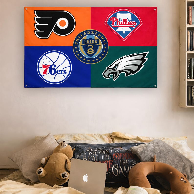 May include: A rectangular wall flag divided into four colored quadrants featuring the Philadelphia Flyers logo in orange, the Phillies logo in red, the 76ers logo in blue, and the Eagles logo in green, with the Philadelphia Union logo in the center.