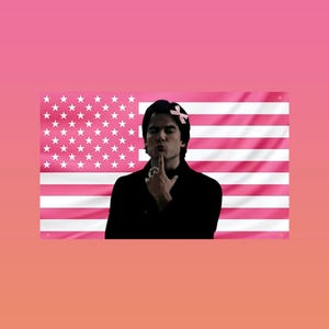 May include: A pink American flag with white stars and stripes is the backdrop for a person in a black coat. The person is wearing a pink bow and has a finger on their lips. The image has a pink and orange gradient background.