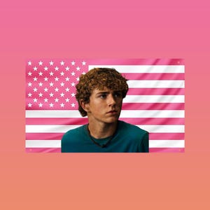 Può includere: Una persona con i capelli castani ricci che indossa una maglietta verde acqua, sullo sfondo di una bandiera americana rosa. La bandiera presenta stelle bianche e strisce rosa, creando una combinazione di colori unica.