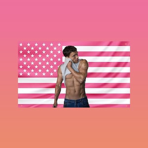 Puede incluir: Una persona con una camiseta sin mangas gris y vaqueros azules está de pie frente a una bandera estadounidense rosa. La bandera tiene estrellas blancas y rayas rosas. La persona se está secando la cara con la camiseta.
